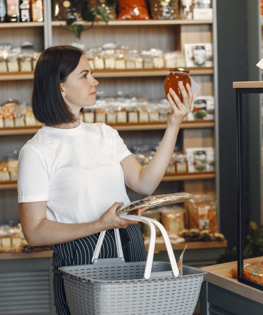 brunette chooses food lady is holding shopping cart girl white shirt supermarket scaled